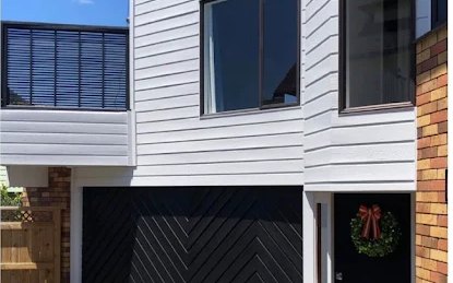 After: 1970s house with orange stained weatherboards, then repainted white with a black chevron garage door
